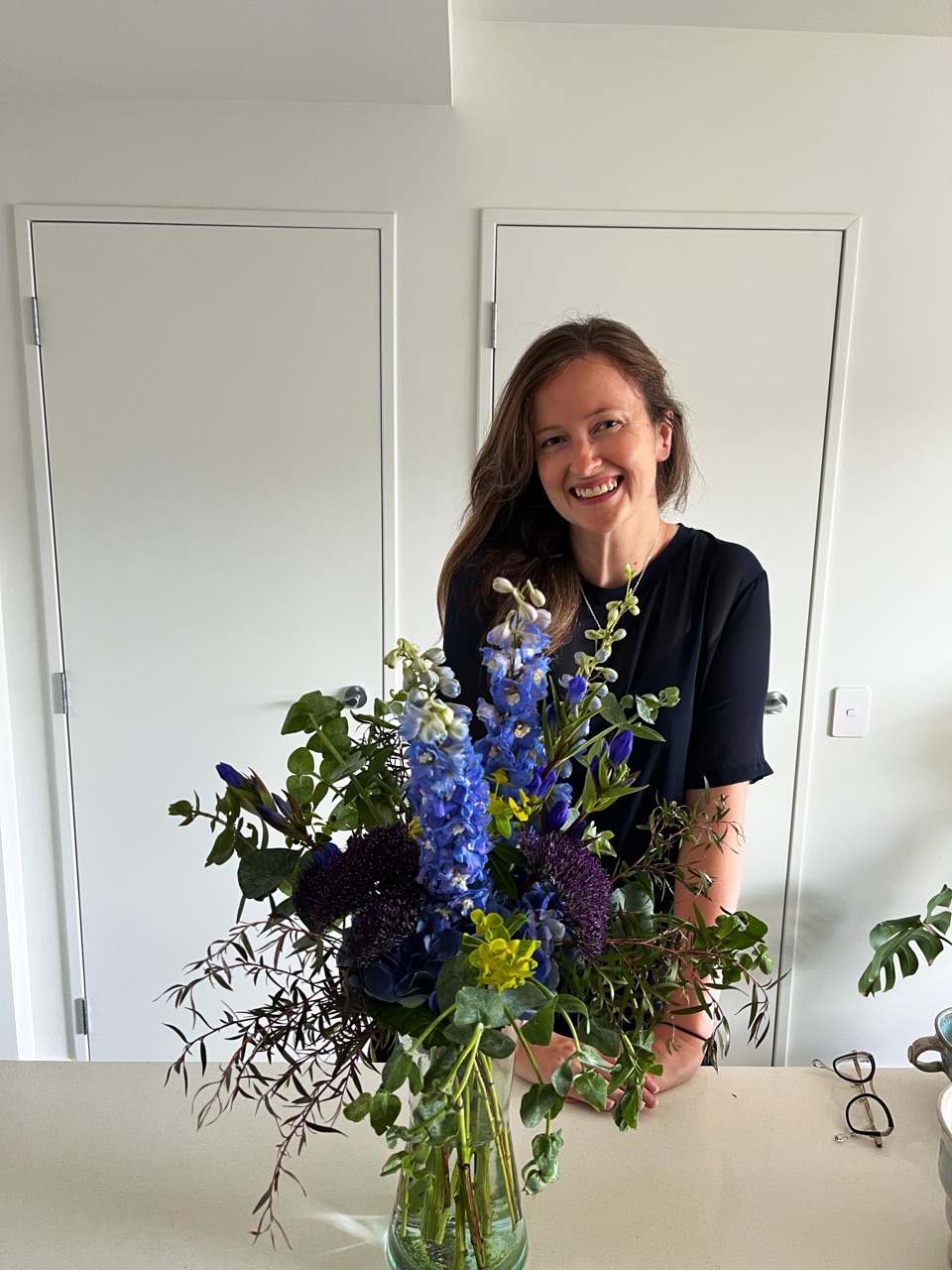 Heather behind a big vase of blue and purple flowers