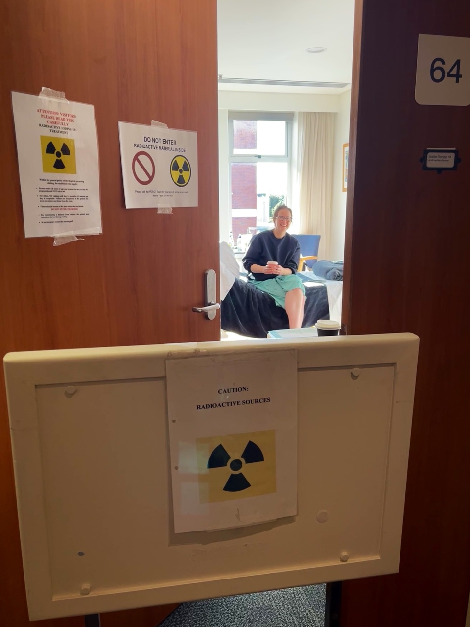 Heather waving from her radioprotection isolation room, door signs in front